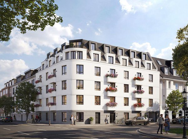 Frontale Außenansicht eines modernen, weißen Mehrfamilienhauses an einer Straßenecke. Das Gebäude besticht durch eine markante, geschwungene Eckfassade, ein graues Sockelgeschoss und ein ausgebautes Mansarddach mit zahlreichen dunklen Dachgauben. An den Fenstern und französischen Balkonen befinden sich dekorative Blumenkästen mit rosa Blüten. Am rechten Bildrand parkt ein brauner SUV, während Passanten auf dem Gehweg die Szene beleben.