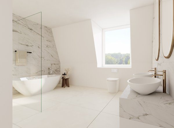 Luxuriöses, helles Badezimmer im Dachgeschoss mit weiß-grauen Marmorfliesen an den Wänden. Links steht eine freistehende, ovale Badewanne hinter einer gläsernen Duschwand. Auf der rechten Seite befindet sich ein Doppelwaschtisch mit zwei runden Aufsatzbecken und eleganten, gold-bronzenen Armaturen unter zwei runden Spiegeln. Ein großes Fenster bringt viel Tageslicht in den Raum.